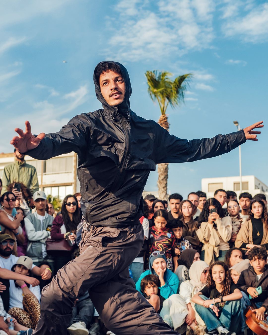 Un danseur en coupe-vent noir, bras ouverts, en plein freestyle debout dans le cercle, en 2026