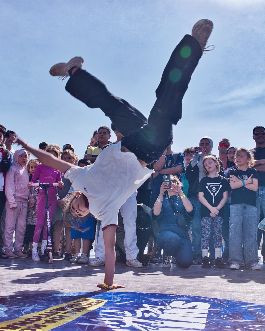 Un danseur figé sur les mains devant le cercle des enfants, en 2026
