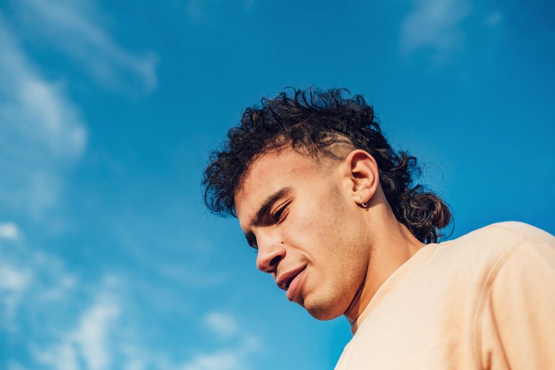 Un jeune danseur, le regard baissé, sous le ciel bleu